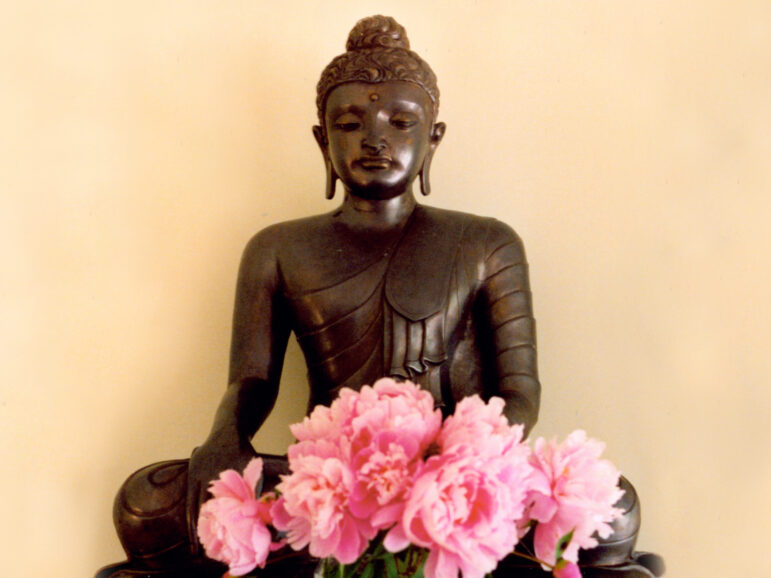 photograph of a bronze Buddha statue with pink flowers in front of it